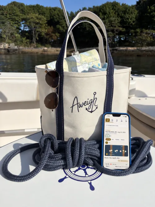 An Aweigh tote bag on the deck of a boat, with a phone beside it showing the Aweigh forecast